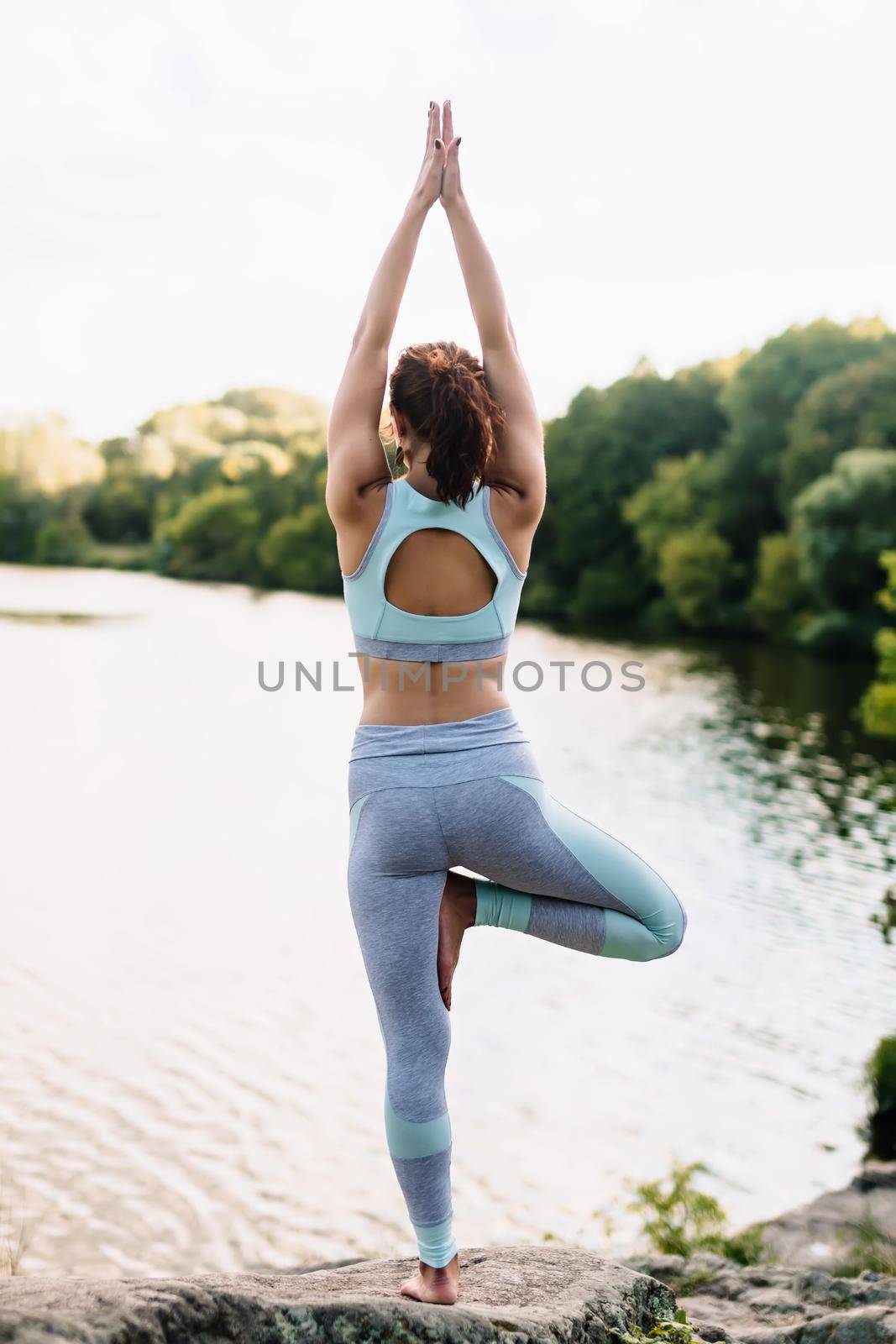 Pretty woman doing yoga exercises in the park on water background