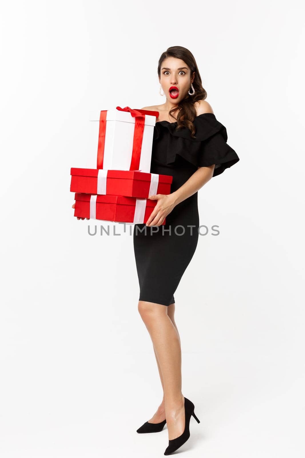 Full length of attractive female model in glamour dress, red lips, holding christmas gifts and looking amazed, receive presents, white background by Benzoix