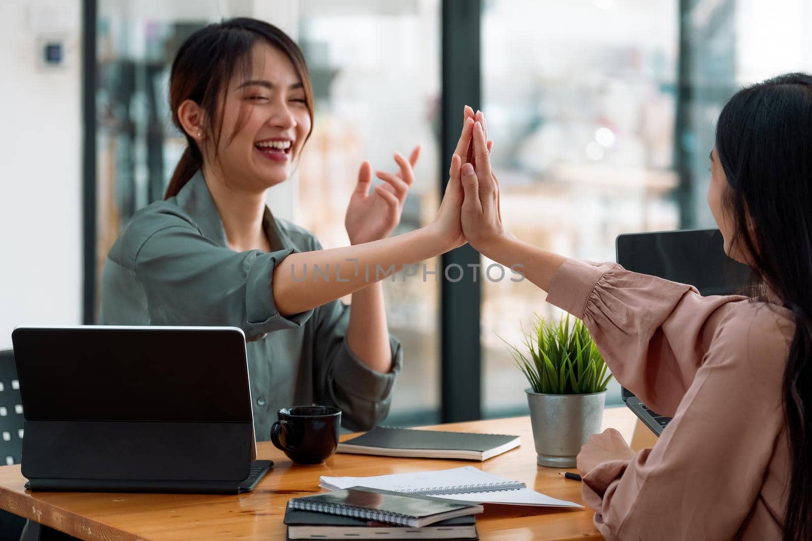 Group of young asian business people giving coworker high five in office celebrating achievement and success. business teamwork concept by nateemee