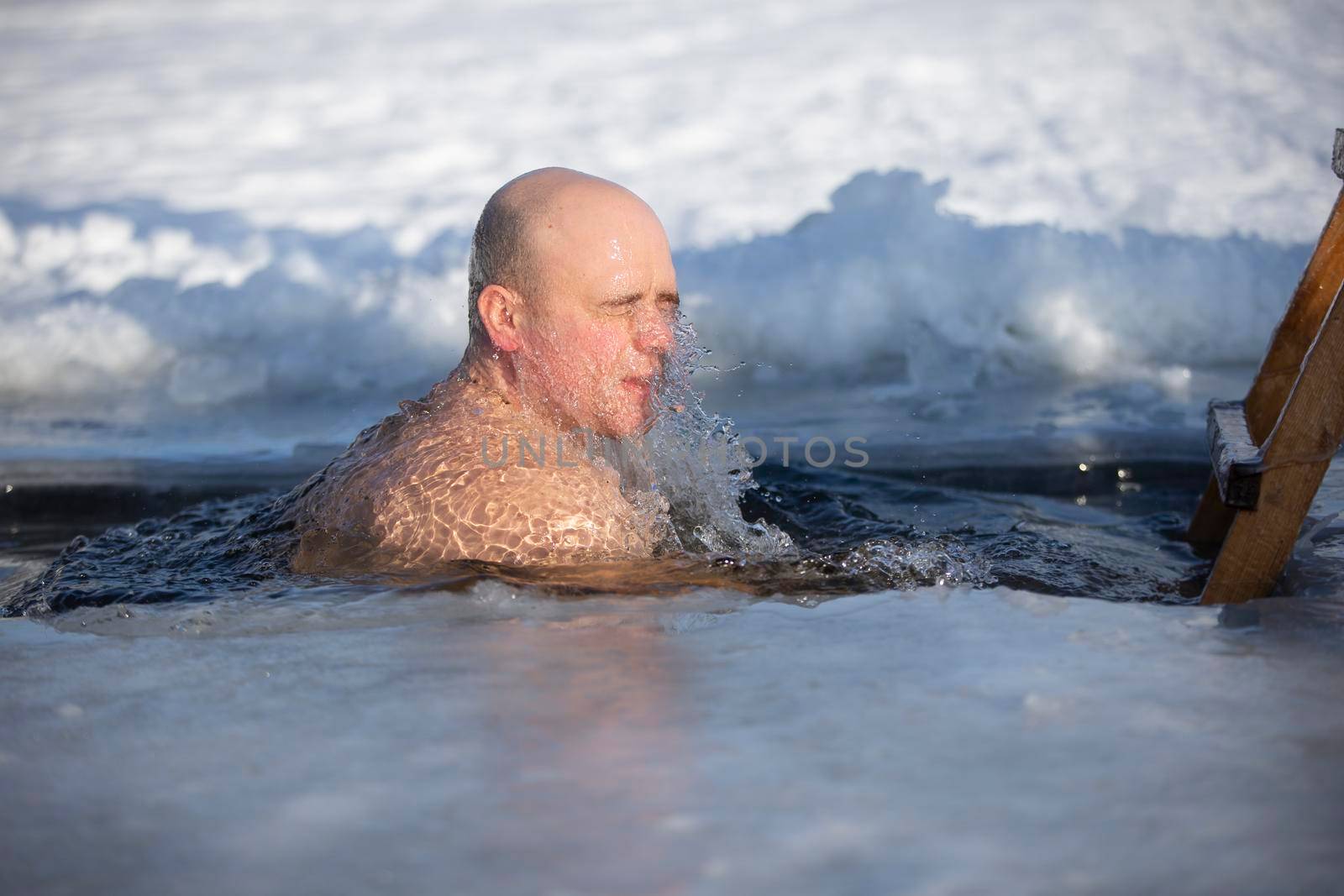 A man plunges into an ice-hole during the winter festival of the baptism of Jesus. A man swims in the ice-hole in winter. Walrus people.