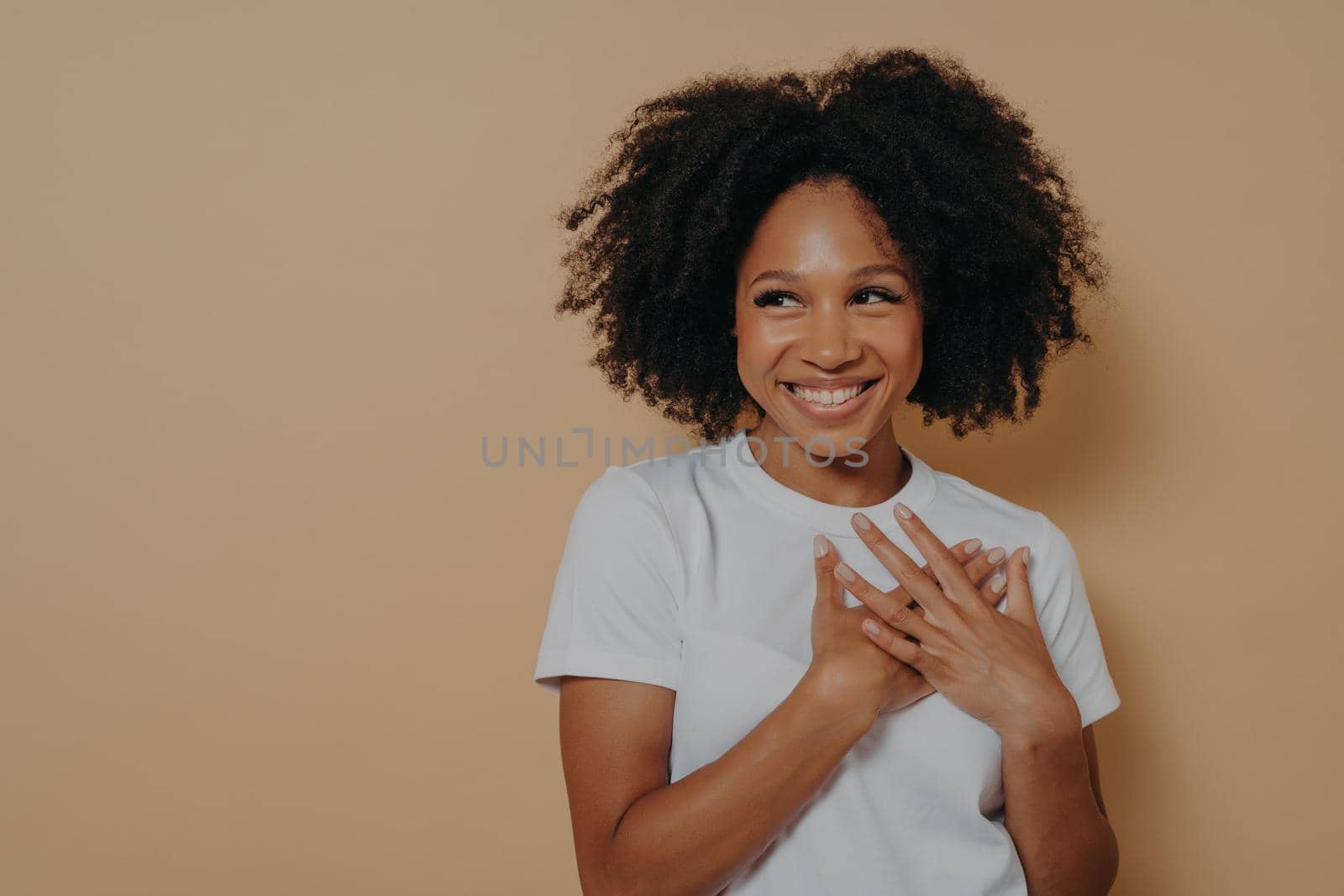 Portrait of happy african woman posing with smile looking away, holding hands on chest by vkstock