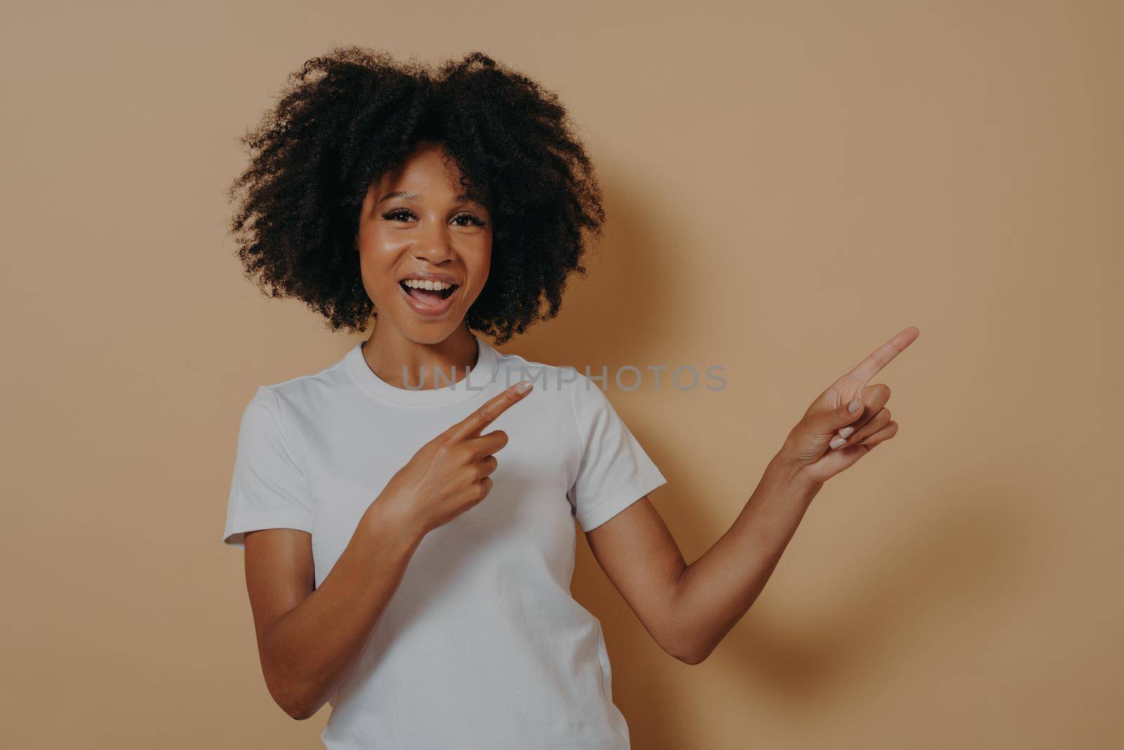Young african american girl wearing casual clothes cheerfully and broadly smiling while pointing with both hands and index fingers up to side with enthusiastic expression on her face, copy space