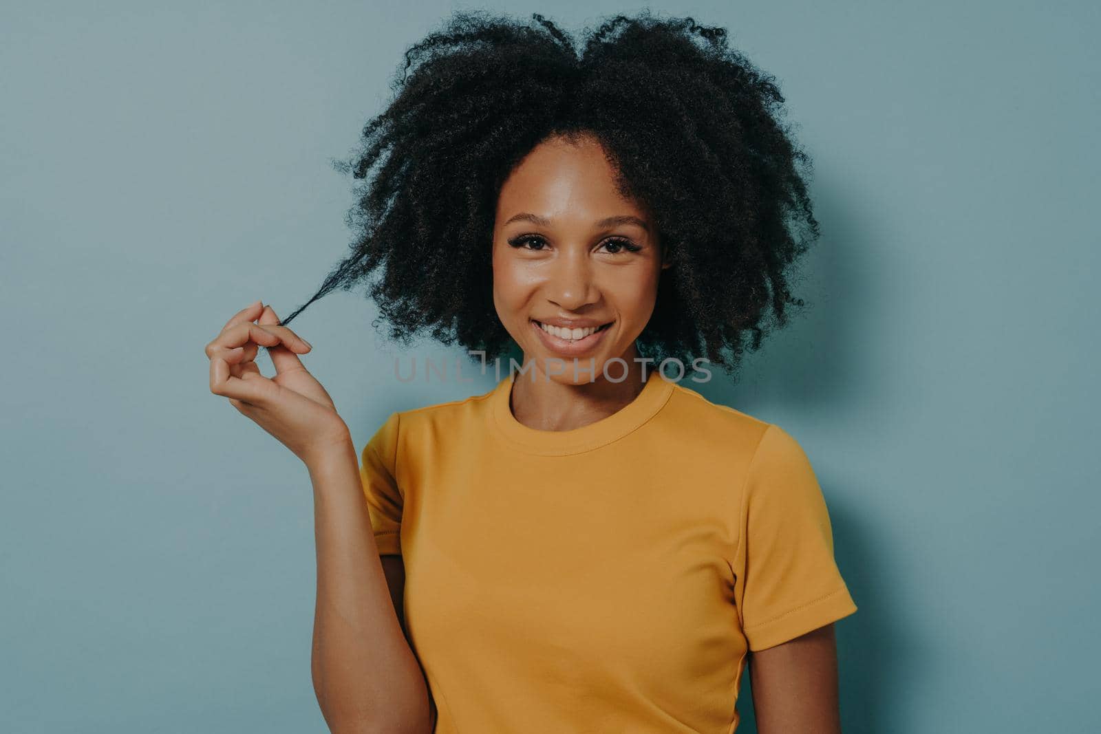 Studio portrait of beautiful young dark skinned woman with shaggy hairstyle smiling cheerfully by vkstock