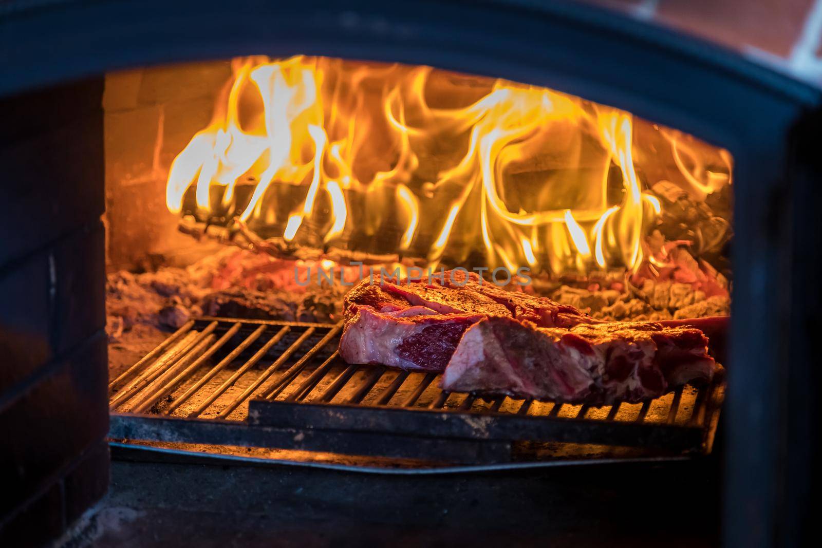 A traditional oven with a burning fire inside for cooking. Inside, raw meat is cooked on the wire rack. Inside view.