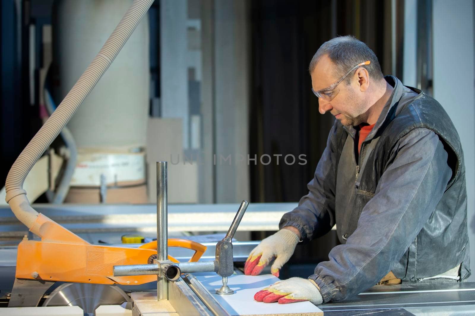 A furniture manufacturing worker at a cutting machine makes furniture parts. Furniture manufacturing.