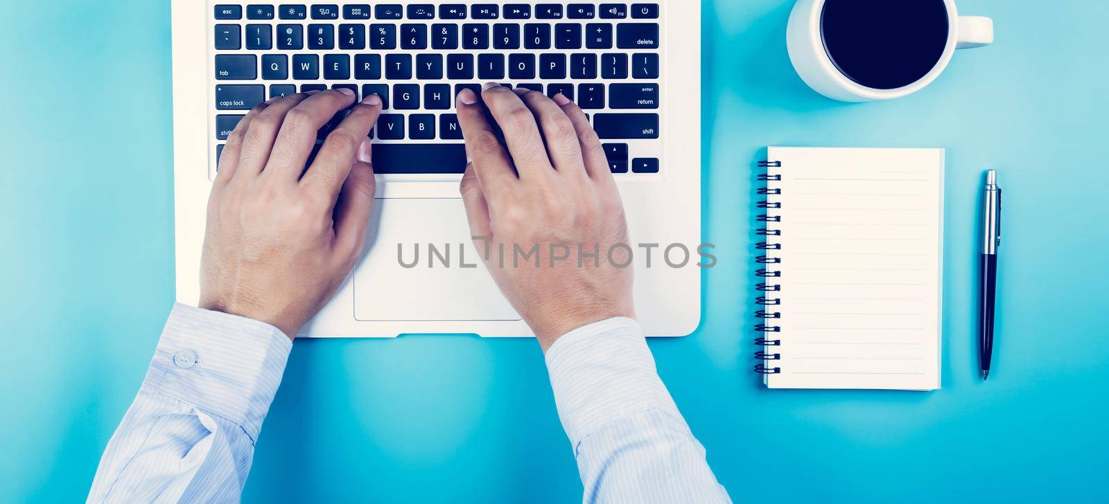 Flat lay, hand of businessman working on laptop computer with cup of coffee on desk in office, workplace and notebook and book on blue background, workspace and copy space, top view, business concept. by nnudoo