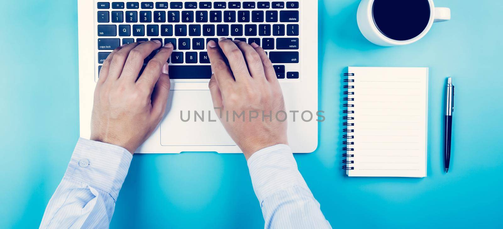 Flat lay, hand of businessman working on laptop computer with cup of coffee on desk in office, workplace and notebook and book on blue background, workspace and copy space, top view, business concept.