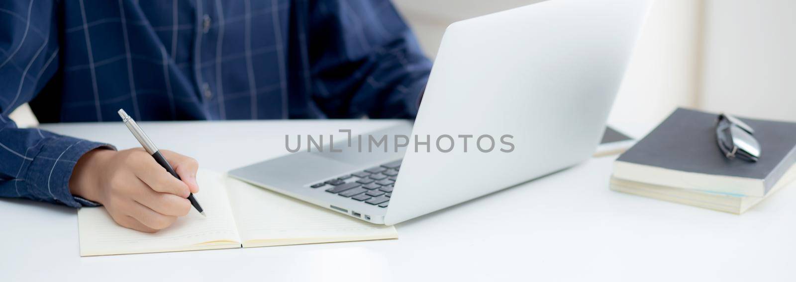 Closeup hand of business man writing on note while using laptop computer on desk at home, male planning on note for business success, author and blog, businessman working on table, employee and job. by nnudoo