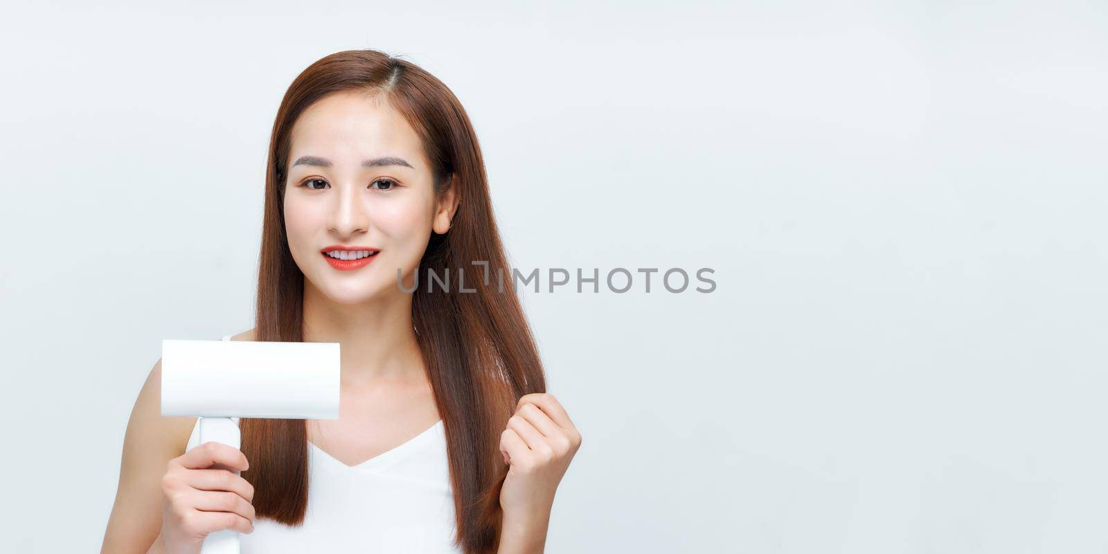portrait of beautiful happy woman drying her long hair with dryer over white background