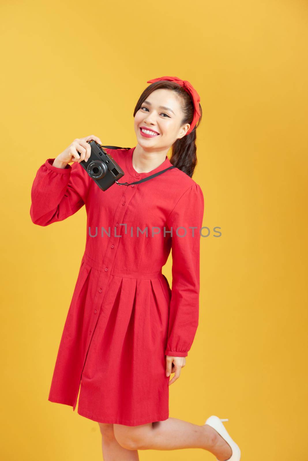 Happy woman tourist travel holding camera isolated on yellow background