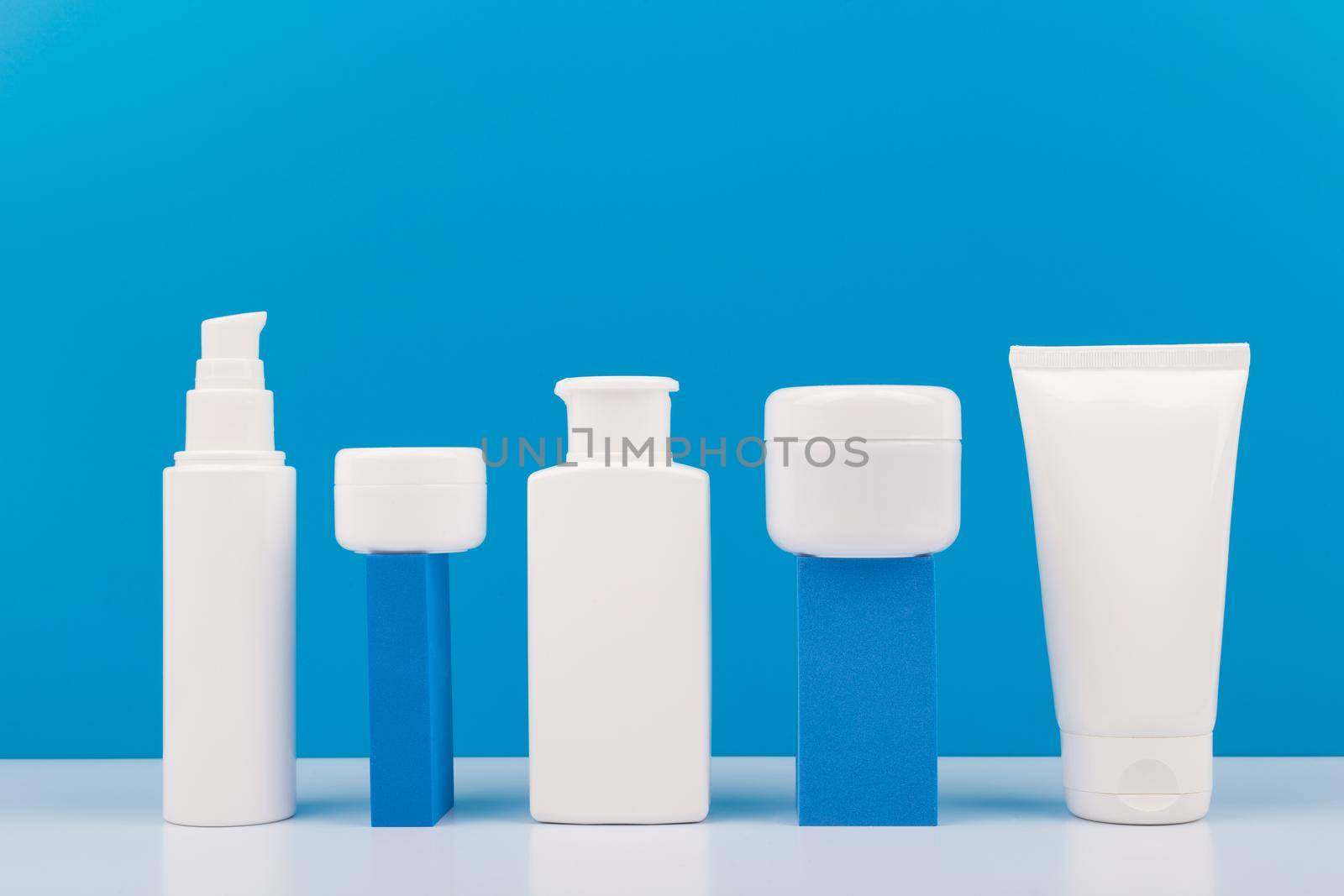Set of white unbranded cosmetic bottles for daily skincare on geometric props for product presentation against bright blue background. Concept of hygiene, man's skin care or anti acne treatment