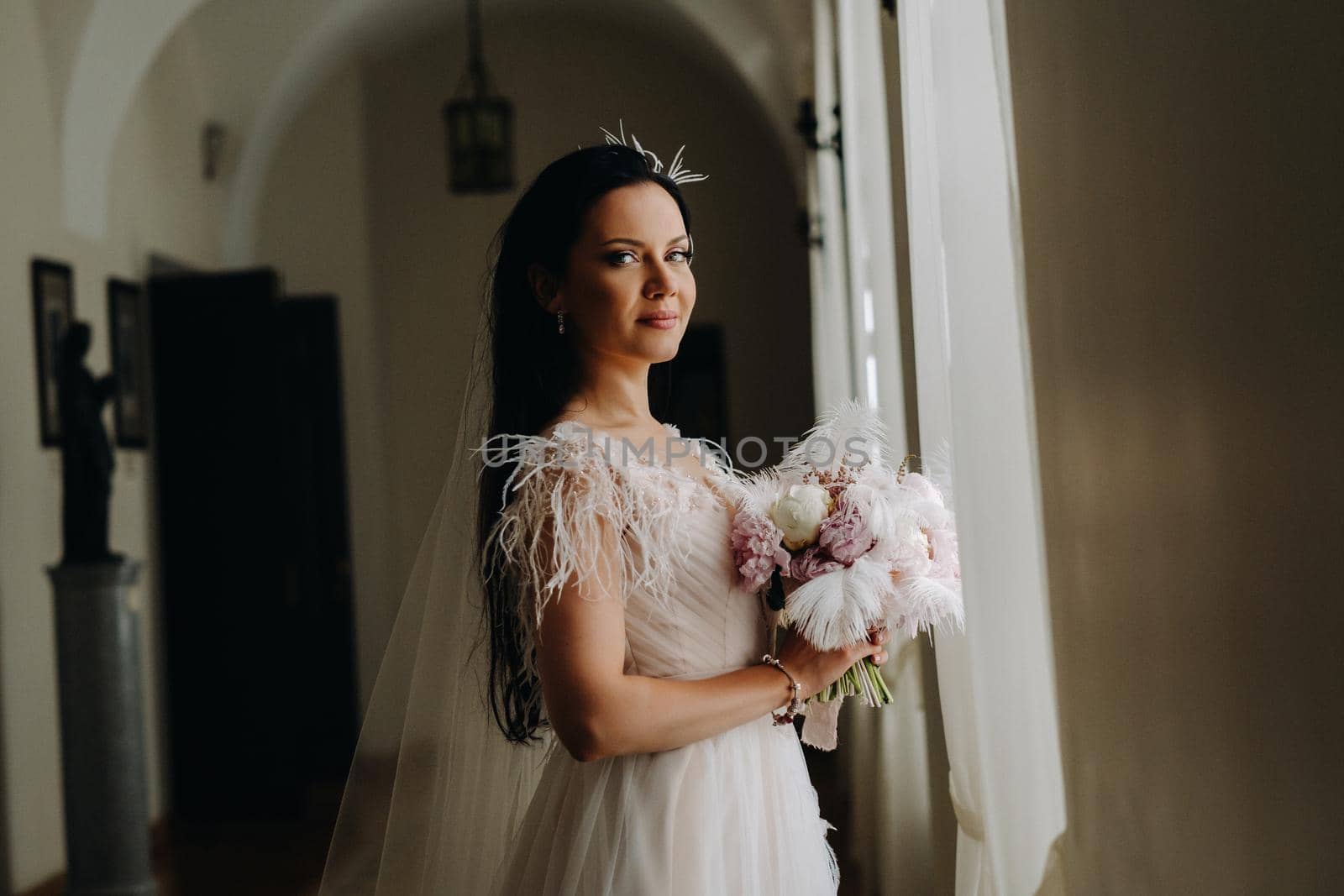 The bride in a wedding dress and with a bouquet stands at the old window and looks by Lobachad