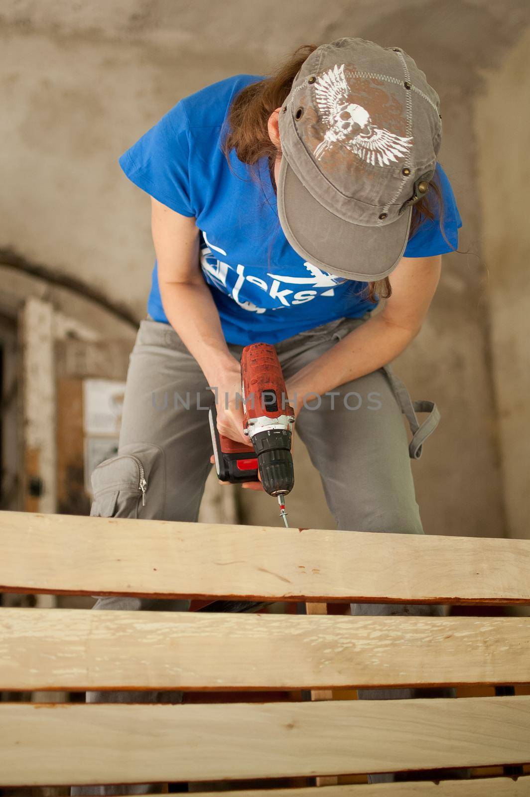 Ukraine, Goshcha, voluntary event, - August, 2021 - skilled young female worker is using power screwdriver drilling during construction wooden bench, gender equality, feminism. by balinska_lv