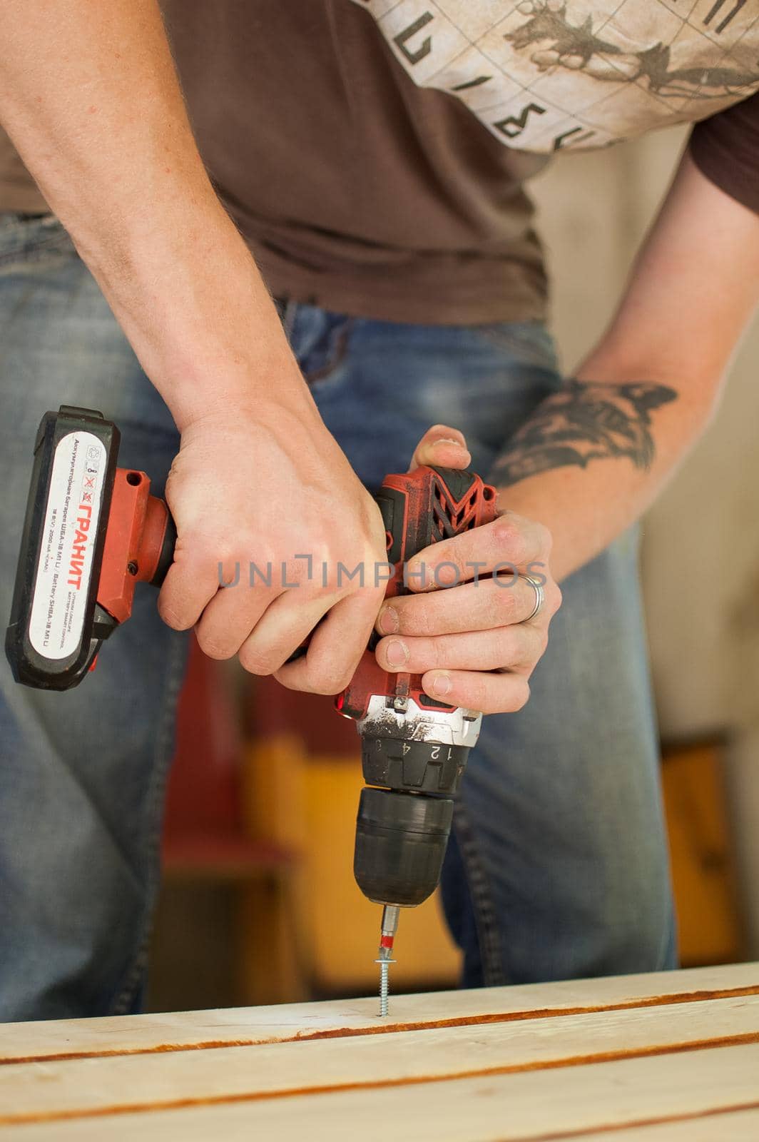 Ukraine, Goshcha, voluntary event, - August, 2021 - skilled young male worker is using power screwdriver drilling during construction wooden bench, do it yourself.