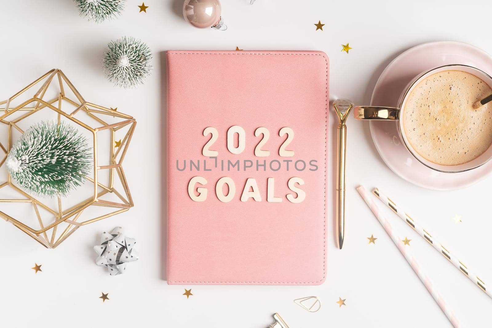 Top view Desktop Christmas pink notepad with 2021goals letters text. Flat lay of white table background with planner, cup of coffee, Christmas decoration, notebook and stationery.