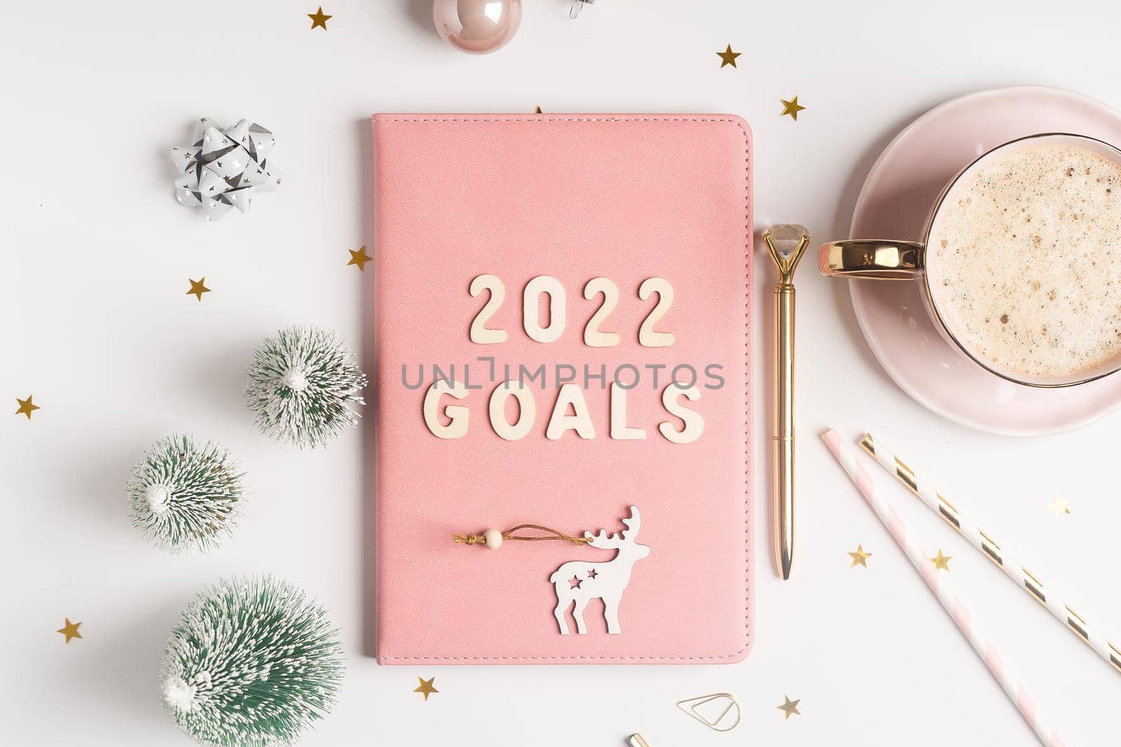Top view Desktop Christmas pink notepad with 2021goals letters text. Flat lay of white table background with planner, cup of coffee, Christmas decoration, notebook and stationery by Ostanina