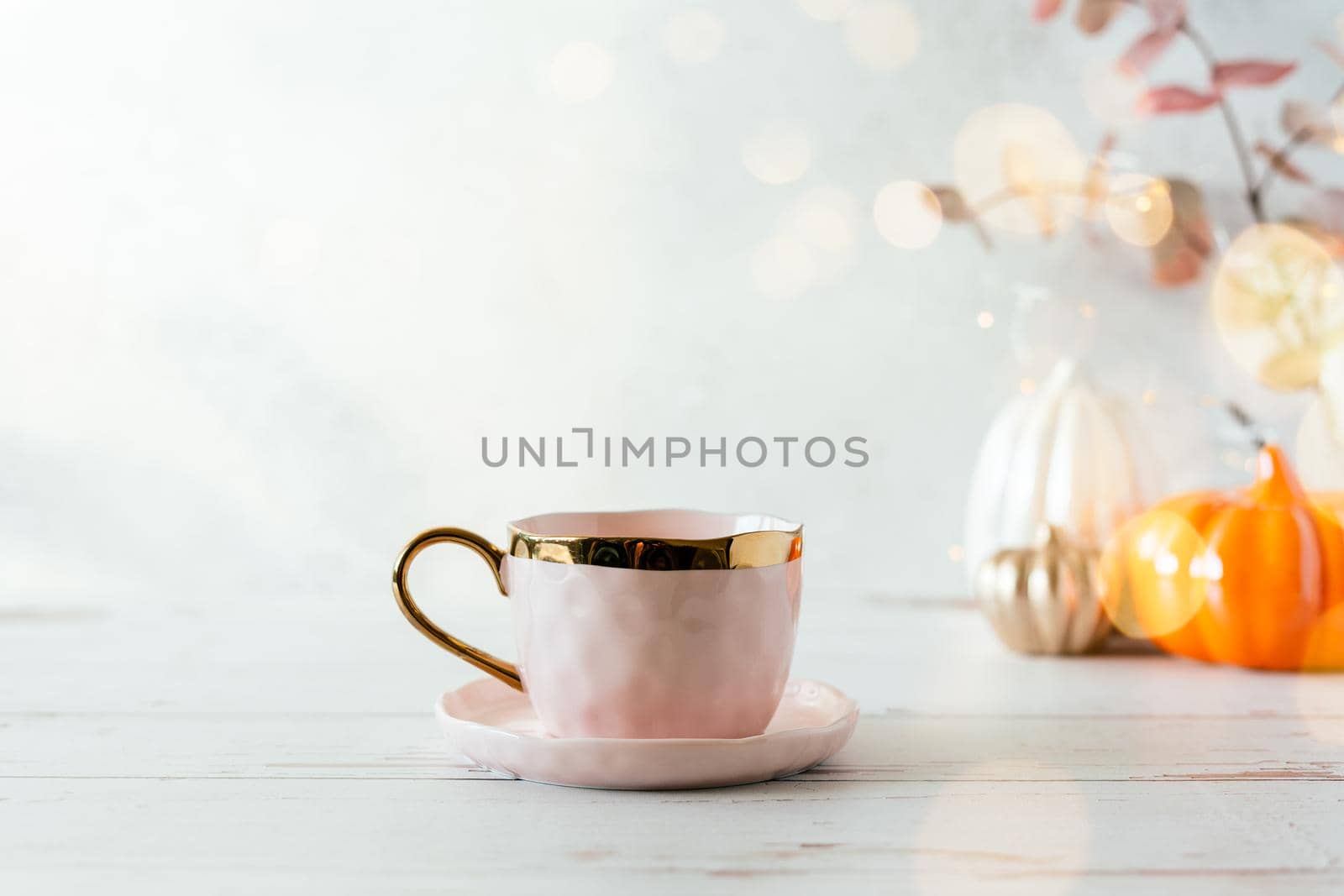 Details of Still life, cup of tea or coffee, pumpkins, candle, brunch with leaves on white table background, home decor in a cozy house. Autumn weekend concept. Fallen leaves and home decoration