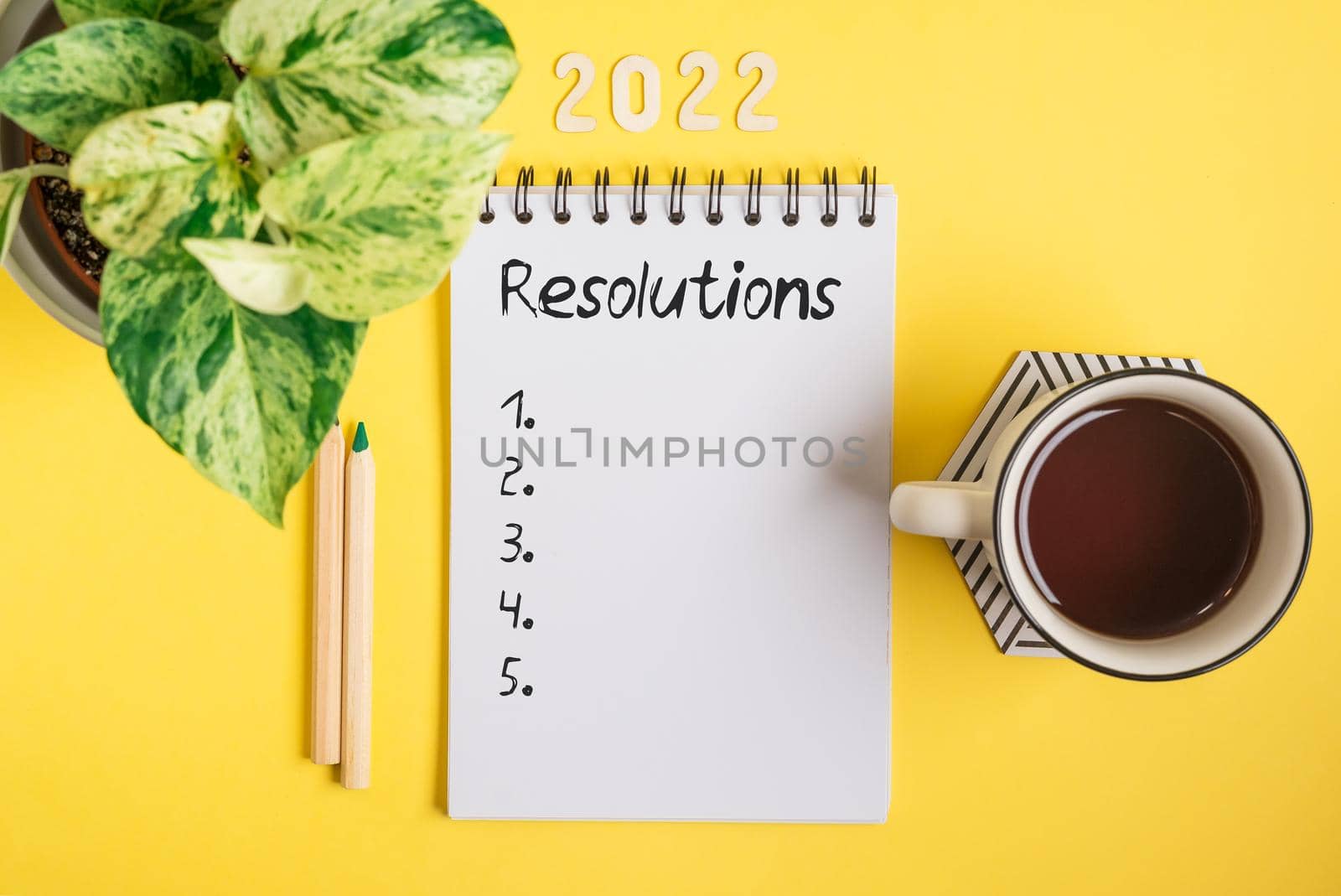 Desktop blank notepad with 2022 resolution text . Flat lay of yellow working table background with cup of tea and plants. Top view mock up