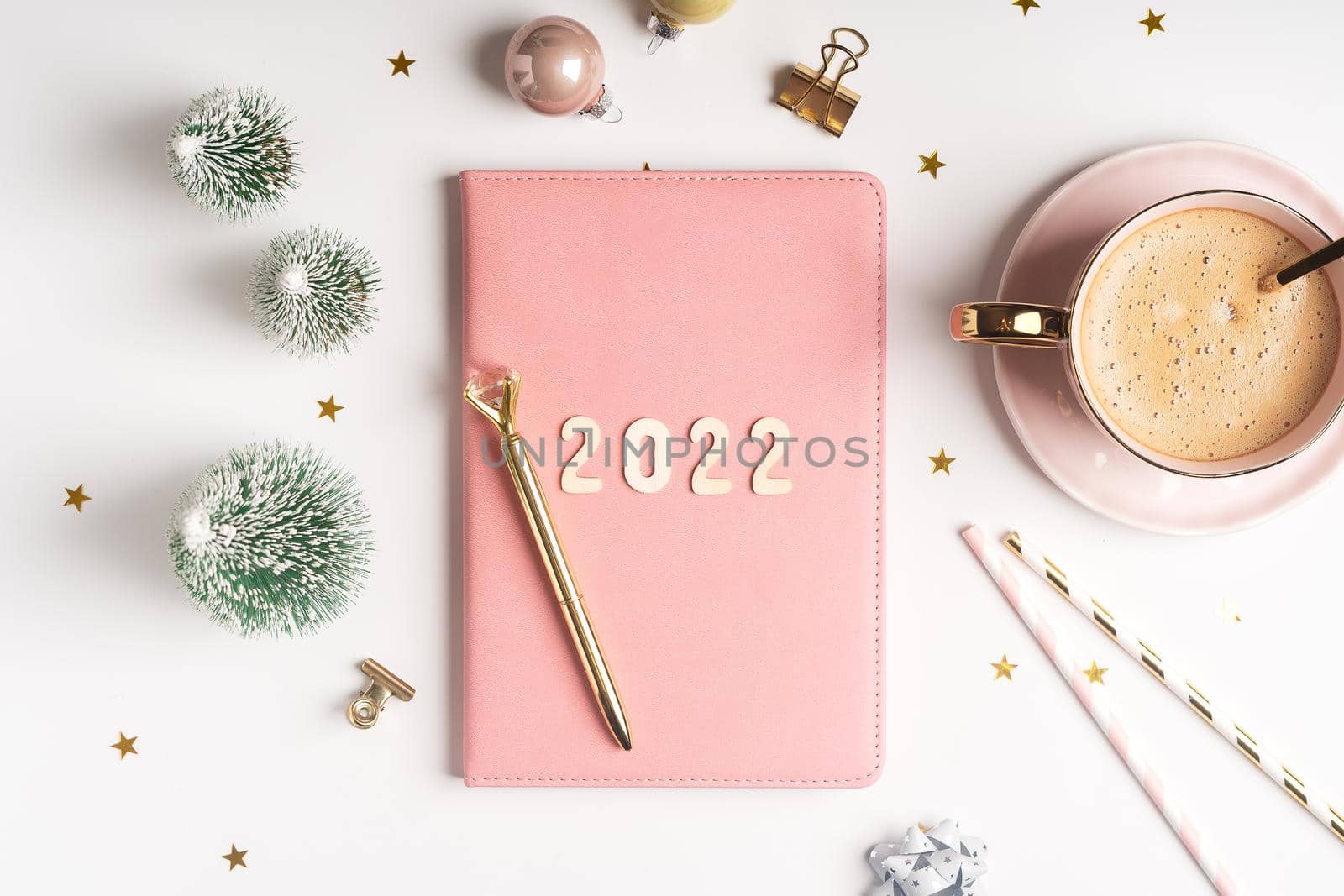 Top view Desktop Christmas pink notepad with 2021goals letters text. Flat lay of white table background with planner, cup of coffee, Christmas decoration, notebook and stationery by Ostanina