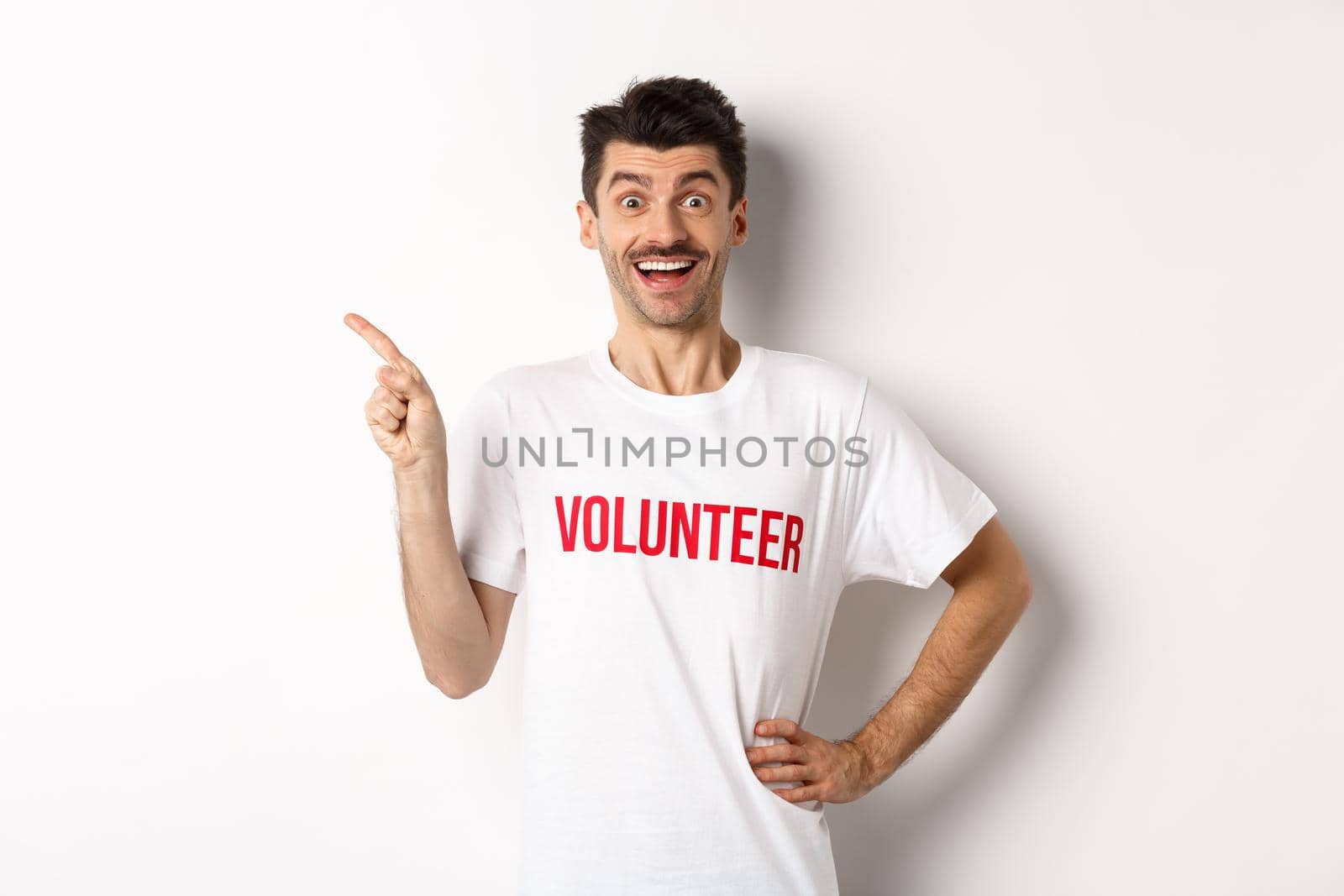 Happy smiling volunteer pointing finger left at copy space, showing announcement, white background by Benzoix