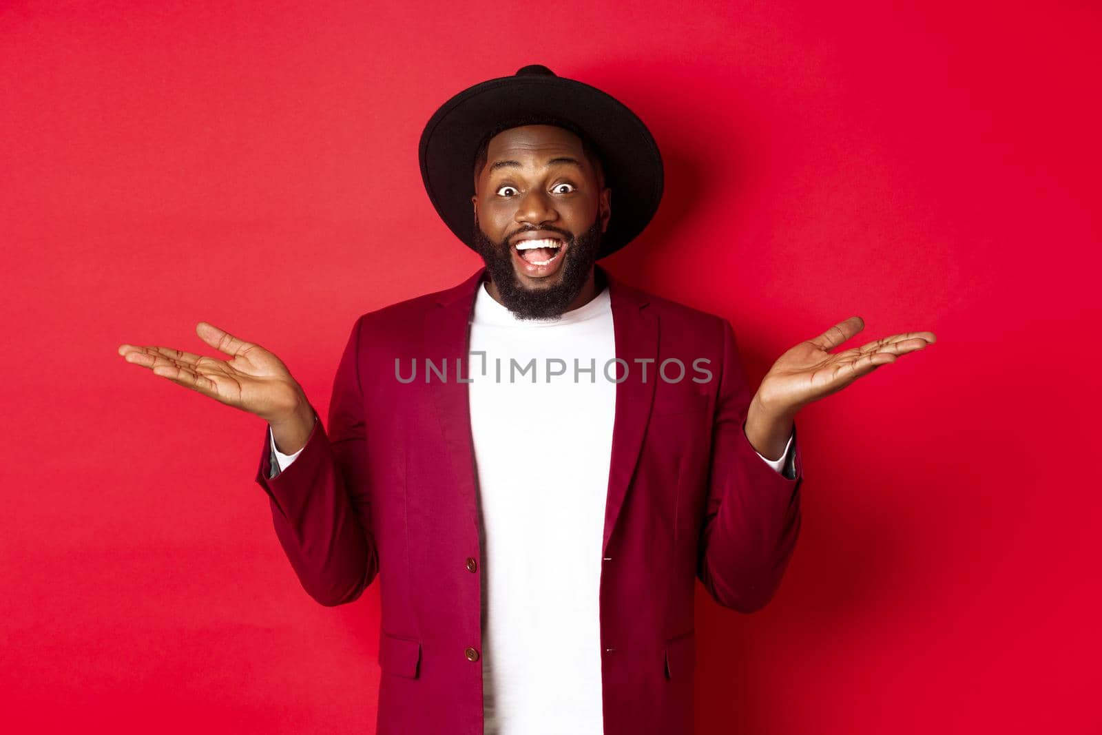 Christmas shopping and people concept. Handsome african american man smiling, spread hands sideways, showing promo offers on copy space, red background by Benzoix