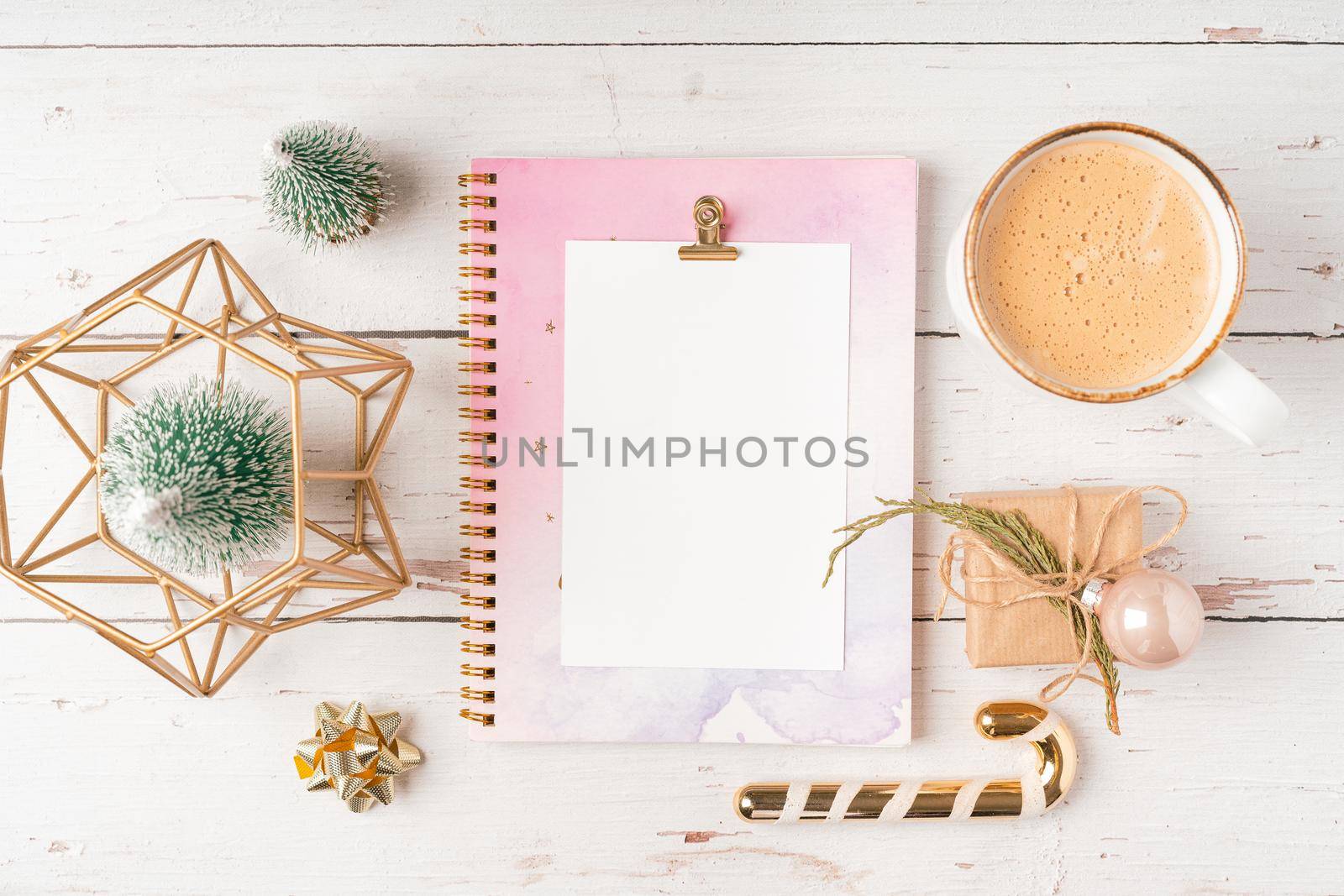 Top view Desktop Christmas notepad with mockup blank paper. Flat lay on white wooden table background with planner, coffee cup, tree brunch, Christmas eco nature decoration, notebook and stationery.