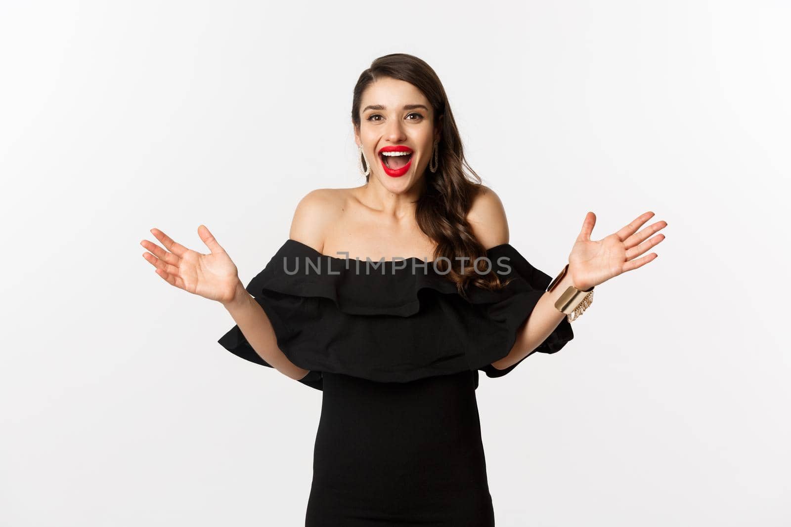 Beauty and fashion concept. Image of surprised and happy young woman in party dress reacting to good news, raising hands up and smiling amazed, white background by Benzoix