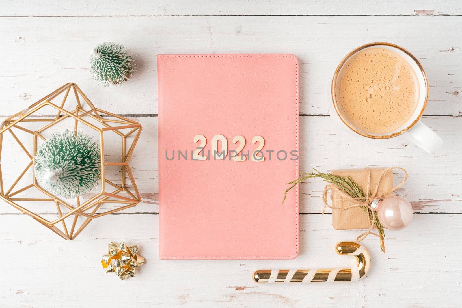 Top view Desktop Christmas pink notepad with 2022 letters text. Flat lay on white wooden table background with planner, cup of coffee, candle, toys, Christmas decoration, notebook and stationery by Ostanina