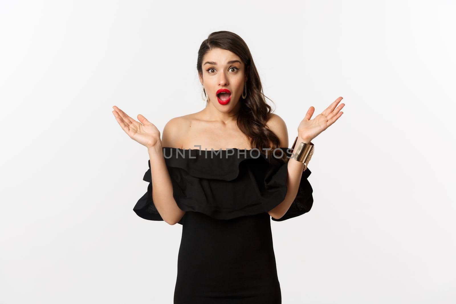 Beauty and fashion concept. Excited beautiful woman looking with amazement at surprise, reacting to good news, standing in black dress with makeup on, white background.