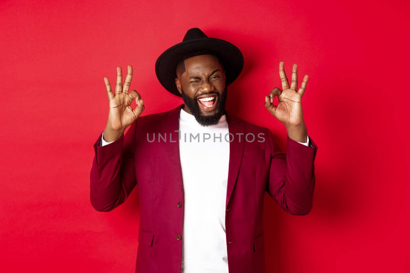 Christmas shopping and people concept. Handsome Black man showing ok sign with confidence, guarantee or agree, saying yes, standing over red background by Benzoix