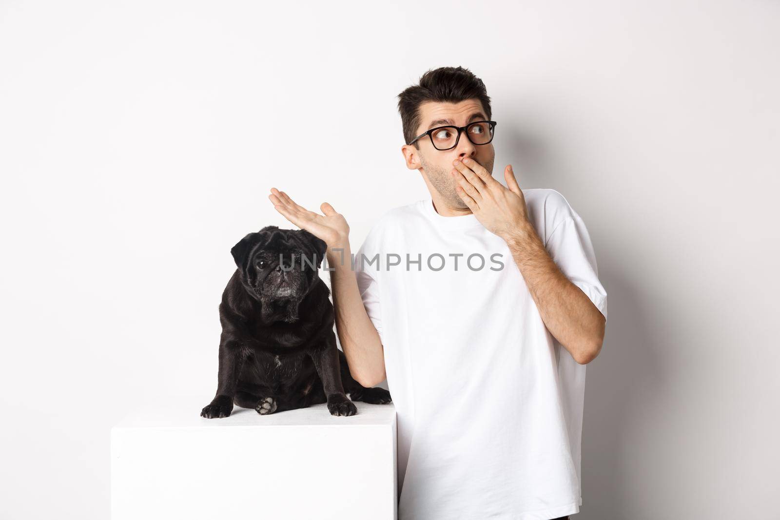 Surprised and shocked man in glasses, standing near cute black dog and staring right at logo, posing over white background.