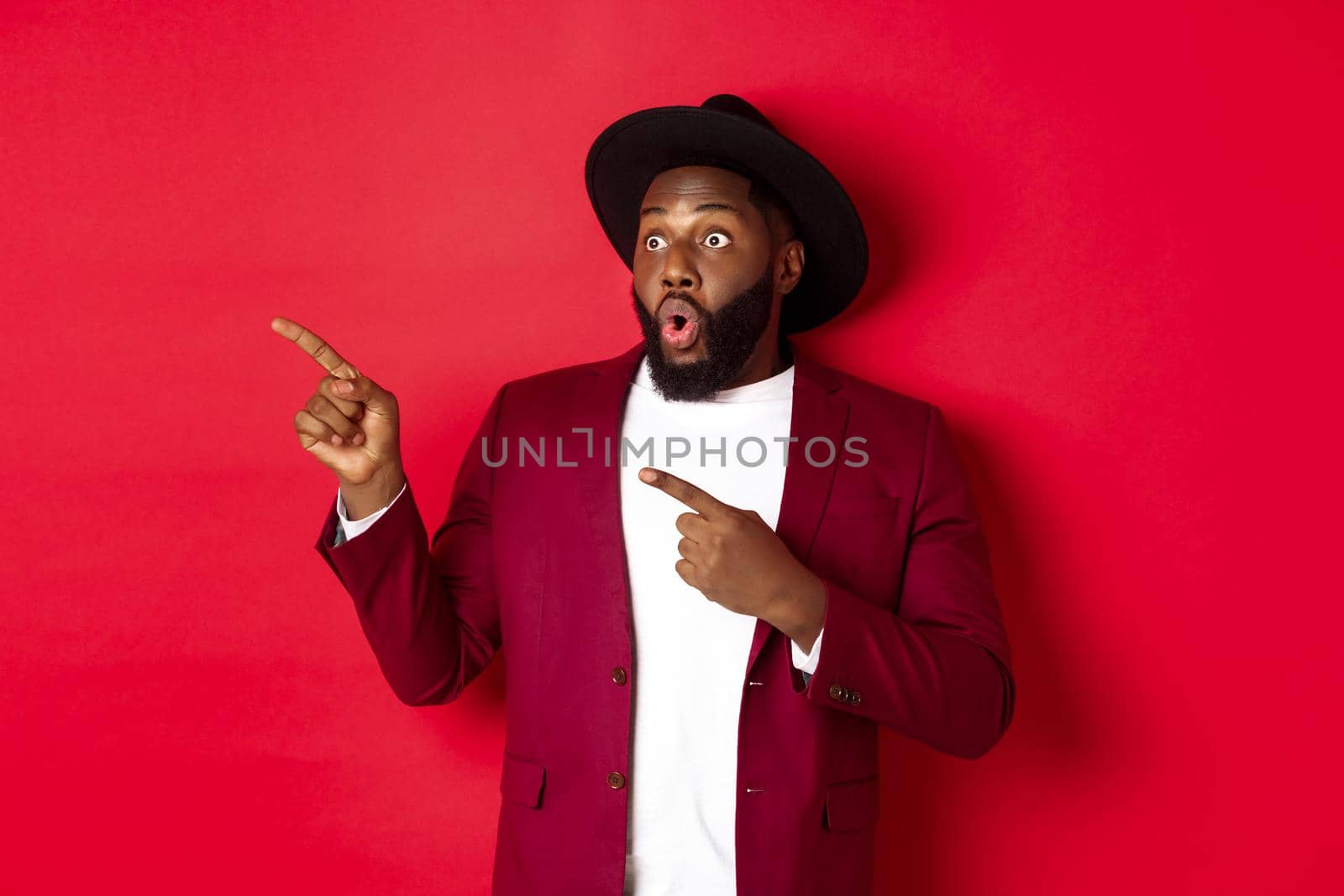 Winter holidays and shopping concept. Happy Black man pointing left and smiling, showing new year promo offer on red background.