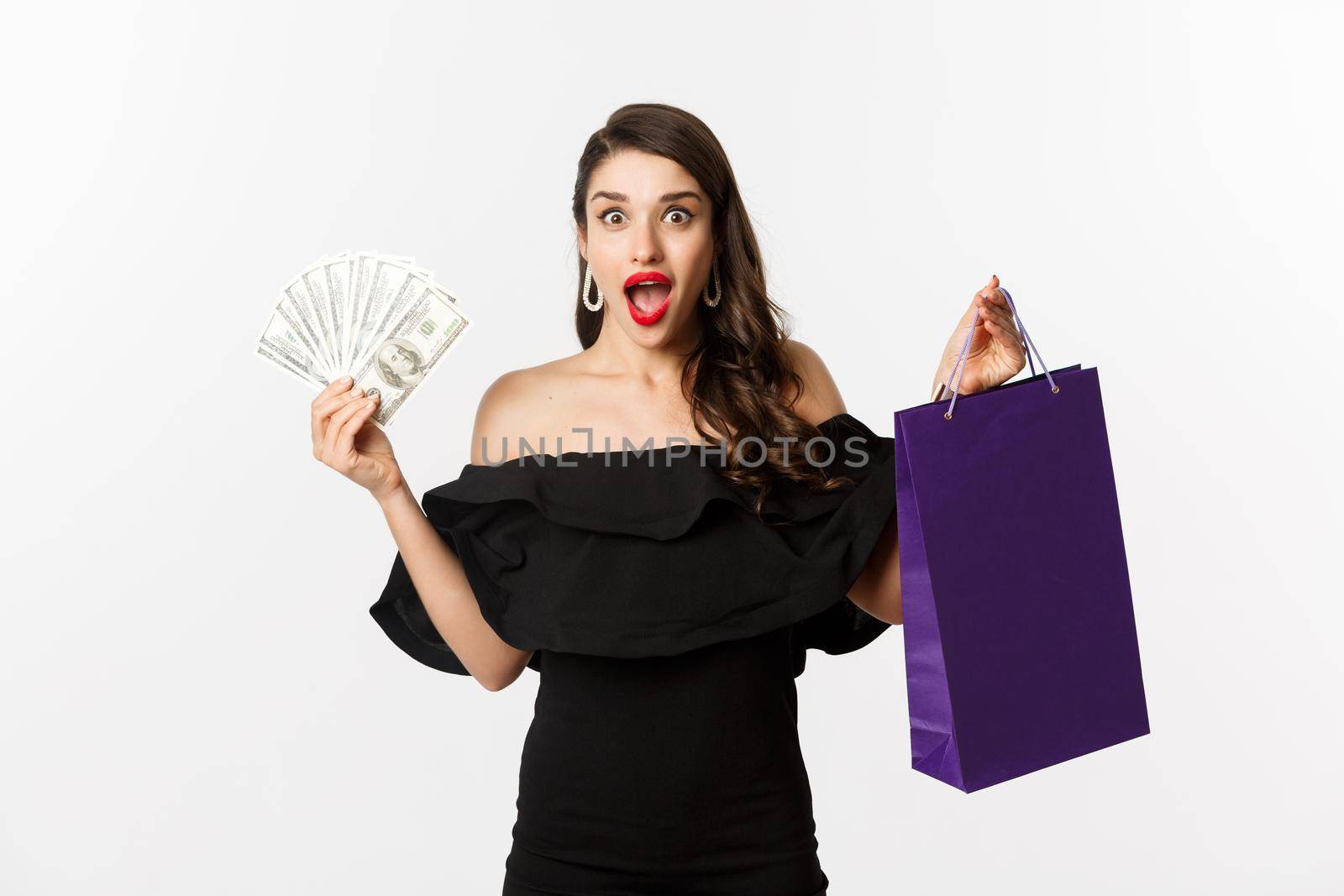 Happy woman buyer holding shopping bag and money, standing in black dress over white background. Copy space