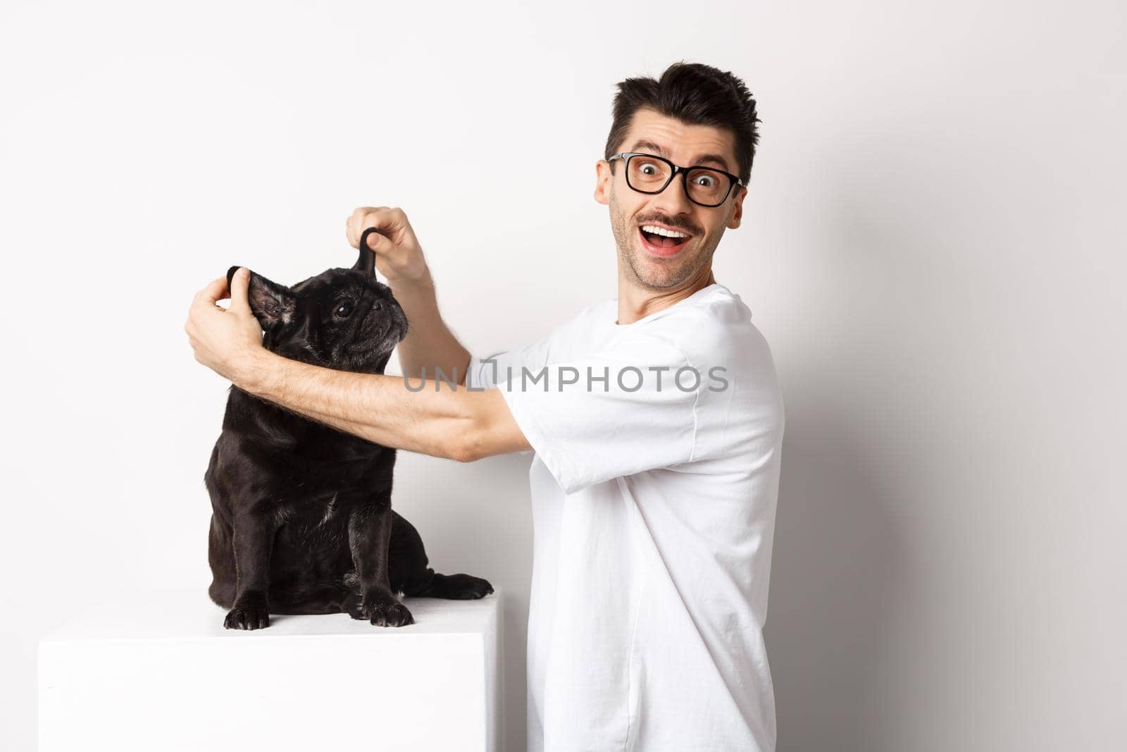 Happy young man looking at camera, showing cute dog ears and feeling rejoice, adopting a pet, standing over white background.