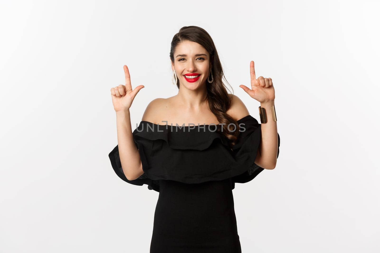 Fashion and beauty. Charming woman with red lips, black dress, smiling happy and pointing fingers up, showing logo, white background by Benzoix