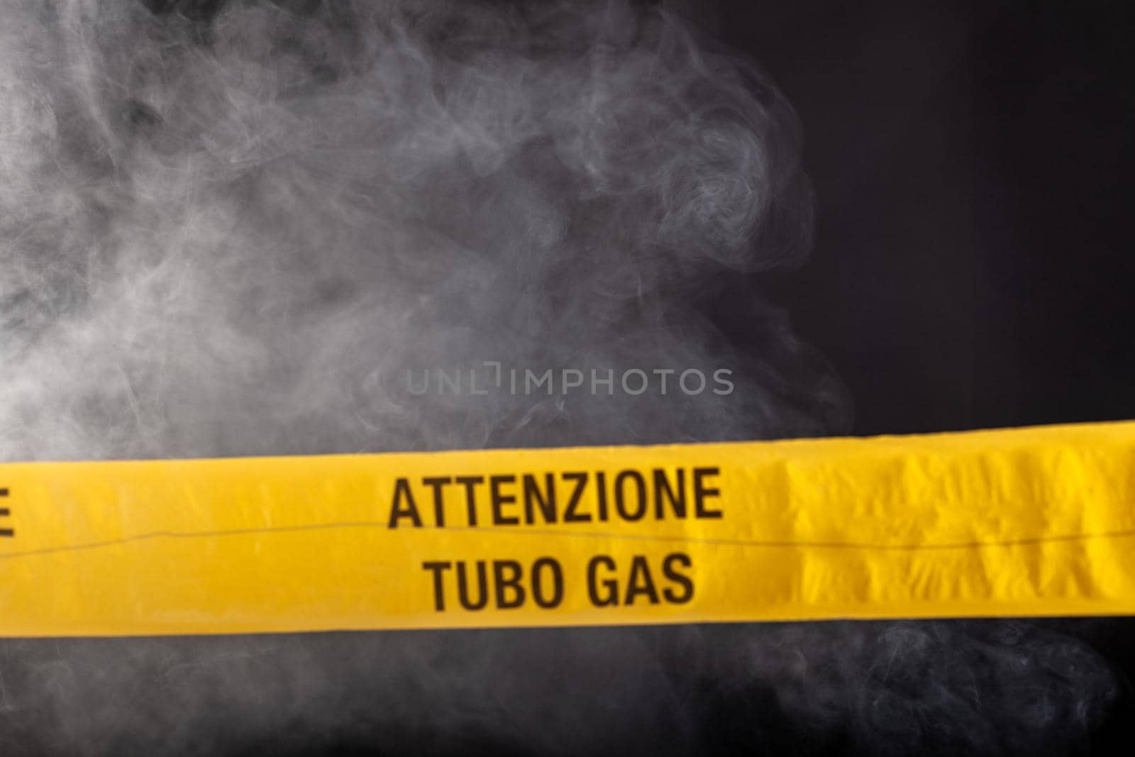 Yellow emergency sign of attention gas pipe on smoke-filled background. On the yellow tape the written notice "attention gas tube"