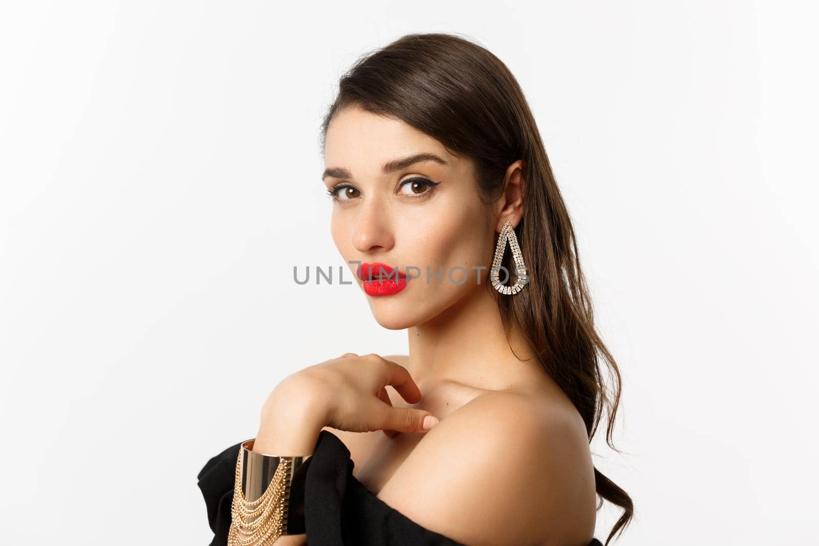Fashion and beauty concept. Close-up of elegant woman with red lips, makeup and earrings, looking at camera self-assured, standing over white background.