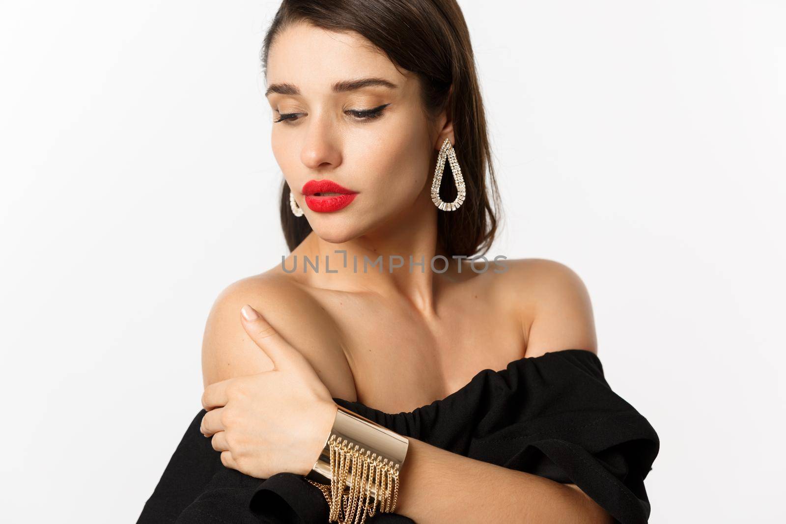 Fashion and beauty concept. Elegant woman with red lips, black dress, showing earrings and jewelry, white background.