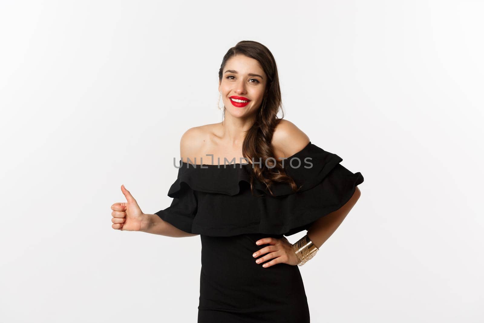Fashion and beauty. Young attractive woman in glamour dress, red lipstick, showing thumb up in approval, recommending something, praise product, white background.