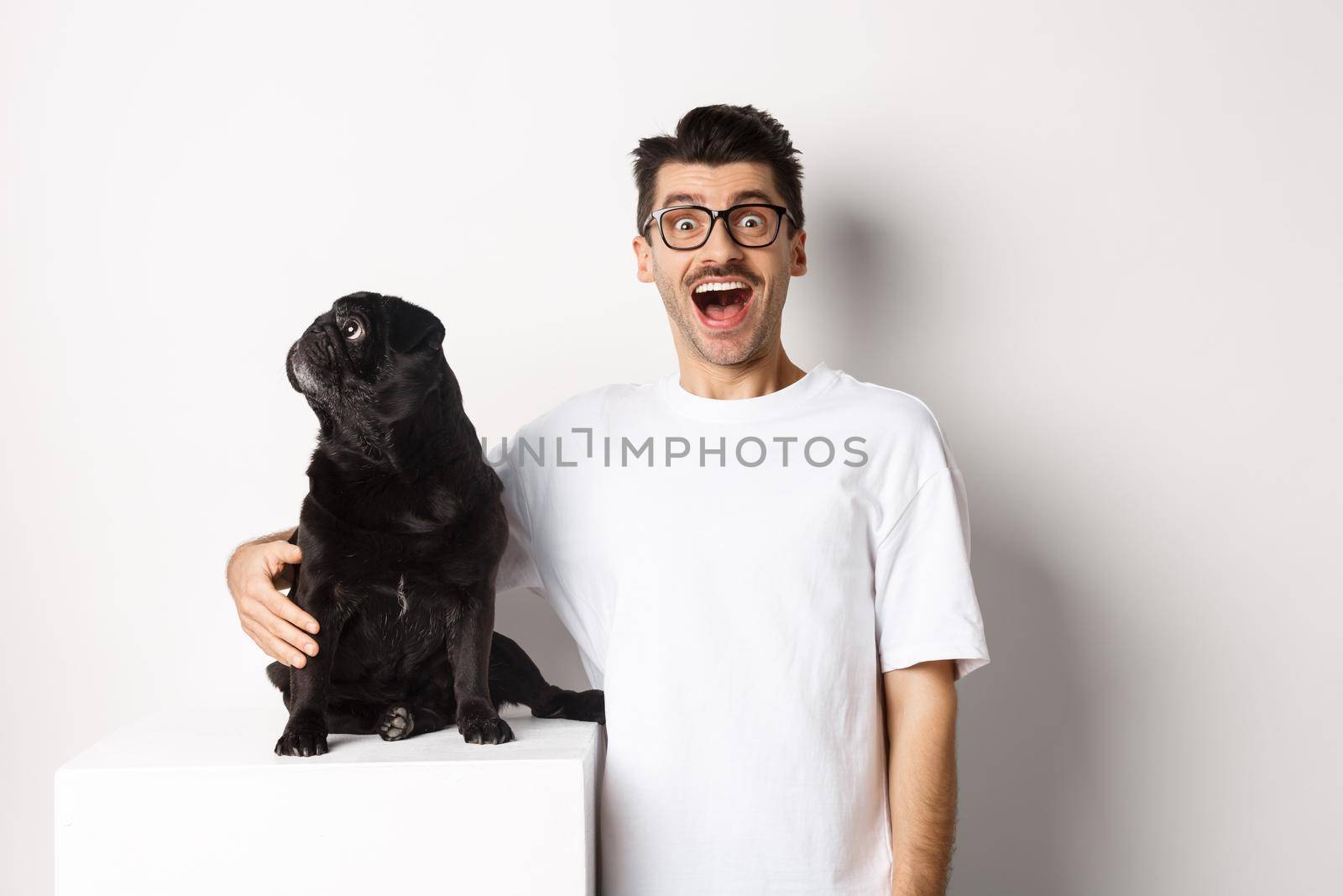 Image of amazed man staring at camera while his small dog looking left at copy space, standing over white background.