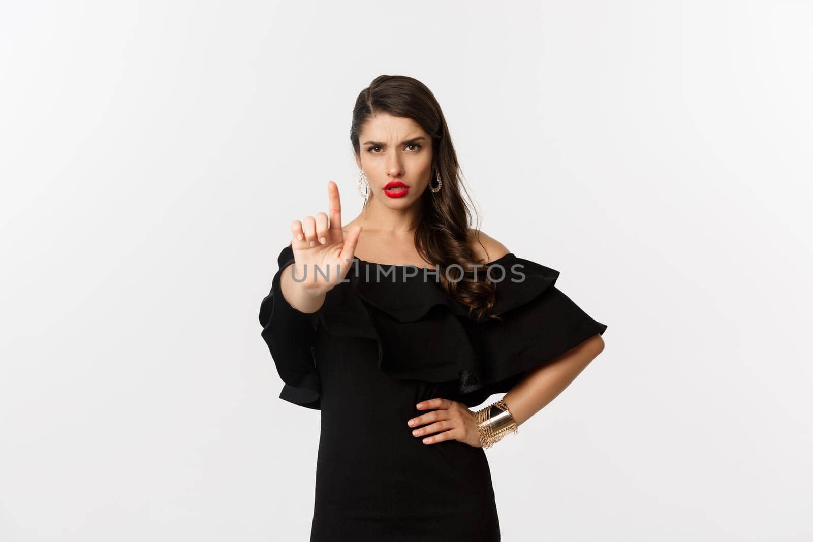 Fashion and beauty. Confident and serious lady in black dress, showing finger in stop gesture, prohibit and disapprove something, standing over white background by Benzoix