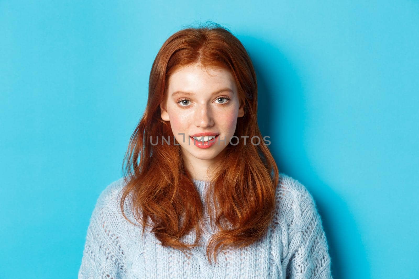 Close-up of young cute redhead girl smiling at camera, standing against blue background by Benzoix