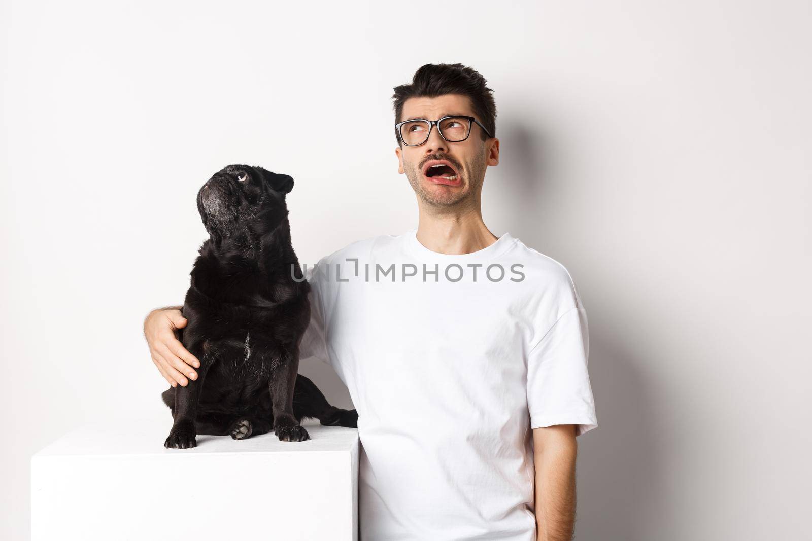 Whining man looking sad while pug staring intrigued at upper left corner, standing against white background by Benzoix