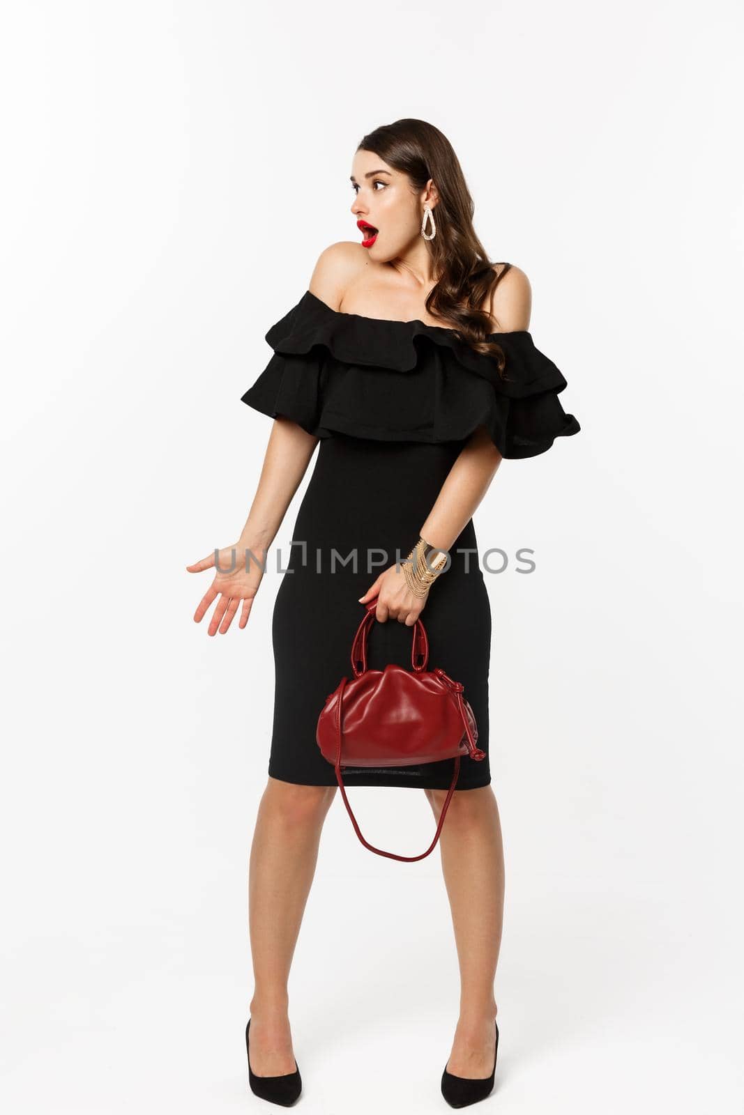 Beauty and fashion concept. Full length of surprised woman in elegant dress, heels looking left confused, holding purse, cant understand what happening, white background.