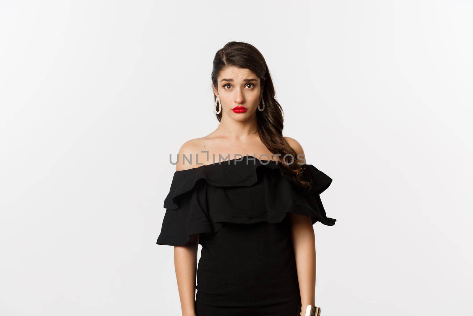 Fashion and beauty. Cute and timid young woman in black dress looking confused and sad at camera, cant understand, standing gloomy against white background.