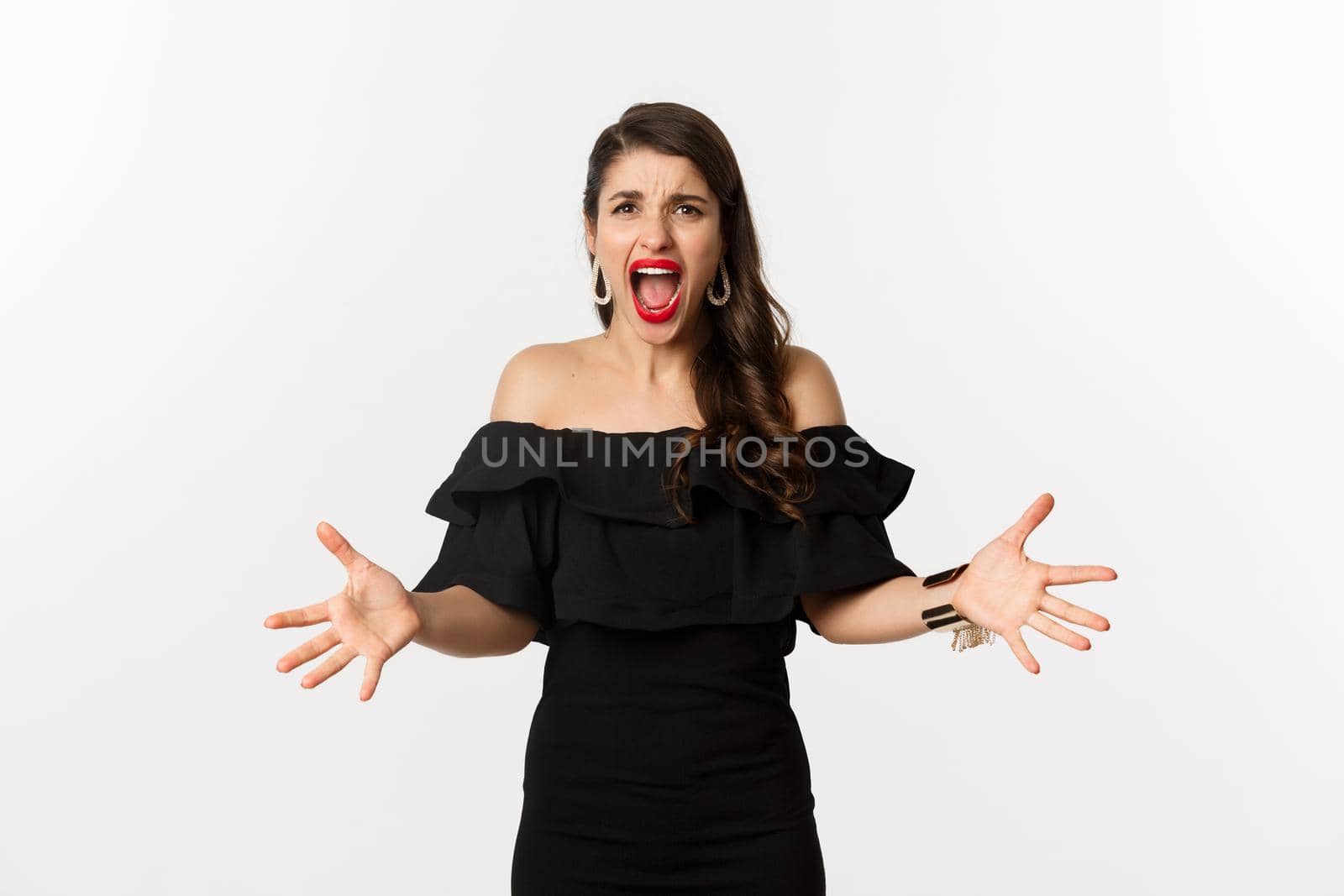 Fashion and beauty. Angry woman in black dress, shouting mad and shaking hands, grimacing outraged at camera, standing over white background by Benzoix