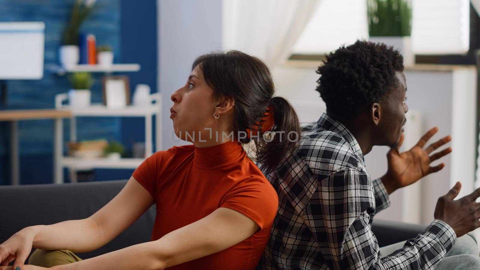 Irritated interracial couple getting into argument on sofa at home. Multi ethnic partners fighting, having relationship problems in living room. Young people sitting on couch yelling