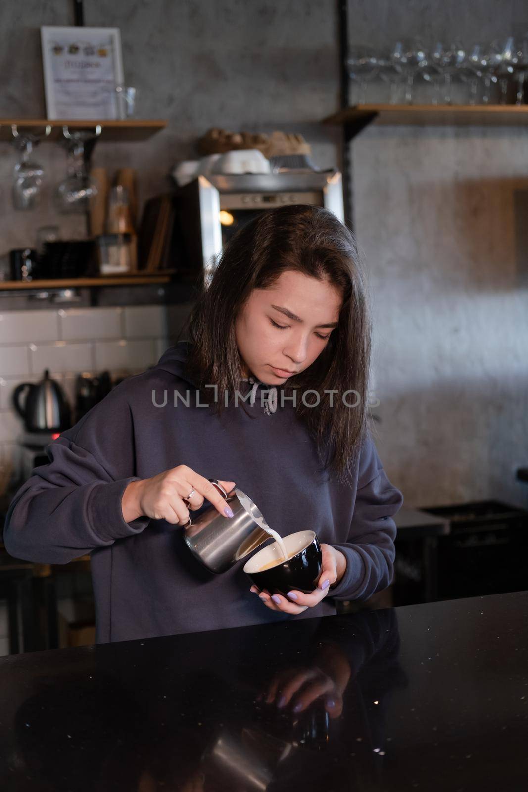 cute girl makes latte in coffee shop. Barista making coffee. Draws a drawing with milk on drink - cappuccino.