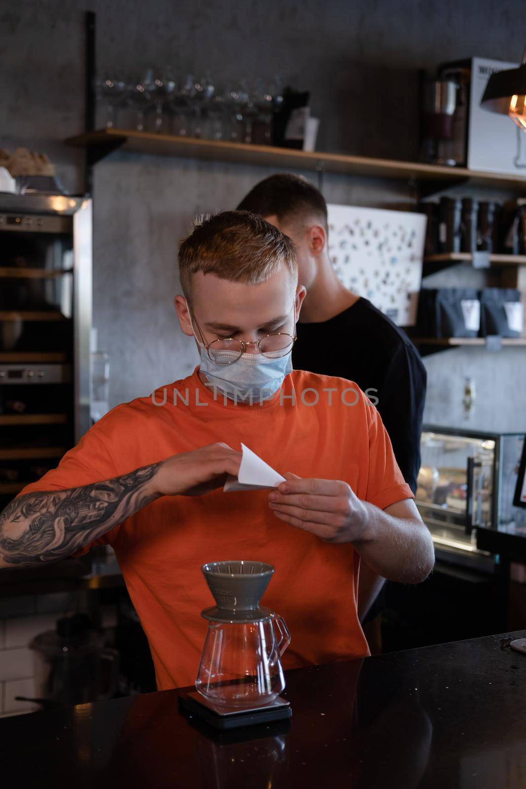 blonde guy in orange t-shirt preparing Alternative coffee brewing: chemex in modern loft coffee shop.