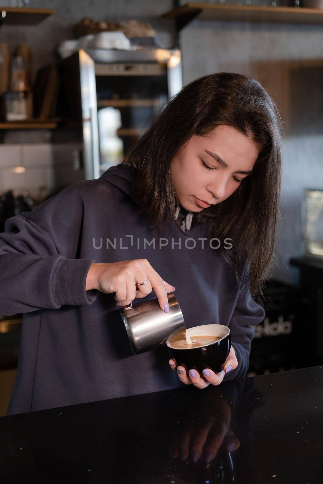 cute girl makes latte in coffee shop. Barista making coffee. Draws a drawing with milk on drink - cappuccino.